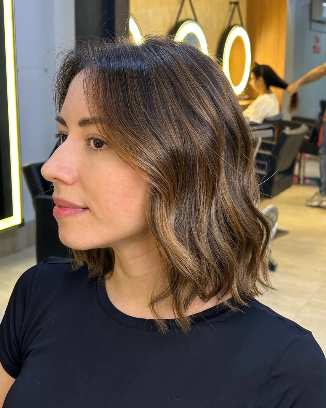 Cliente com morena iluminada no salão do 730, com os espelhos de aro de luz ao fundo